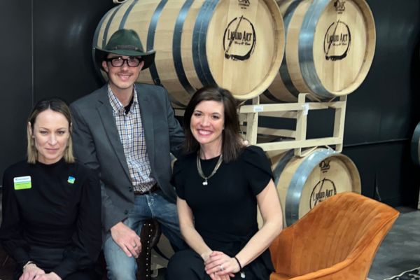 Dave and Dani sitting with Sarah Kephart in front of a tower of wine barrels, all smiling for the camera.