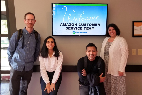 The amazon team smiling in front of a welcome sign.