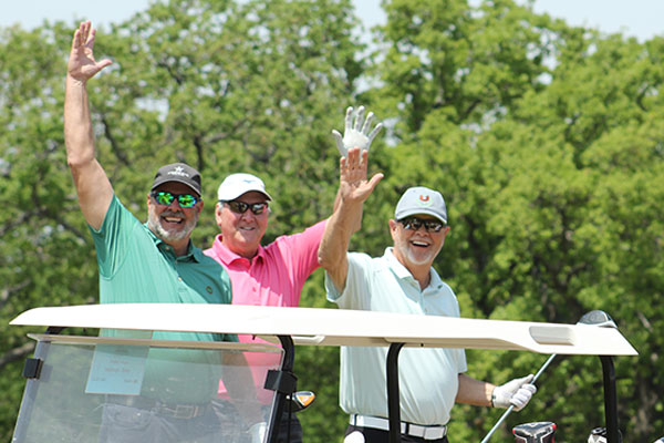 Golfers waving at the camera as they get into their golf cart at the Golf Fore Vision tournament in Dallas.