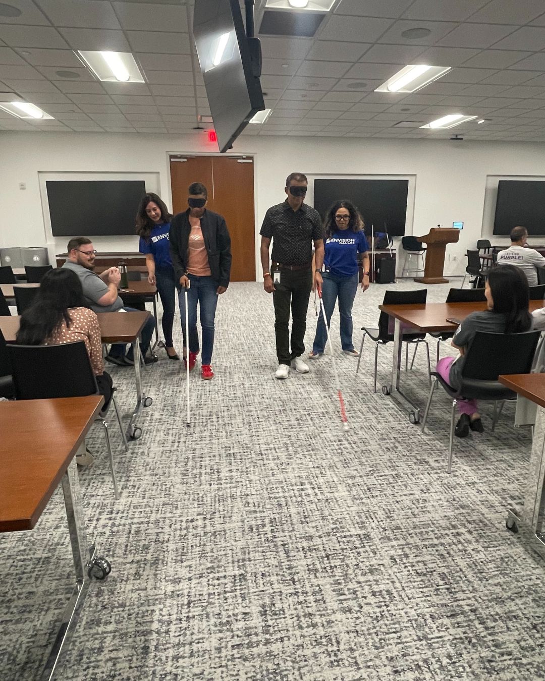 Two Envision employees sight guiding two sighted individuals who are wearing blindfolds and using white canes.