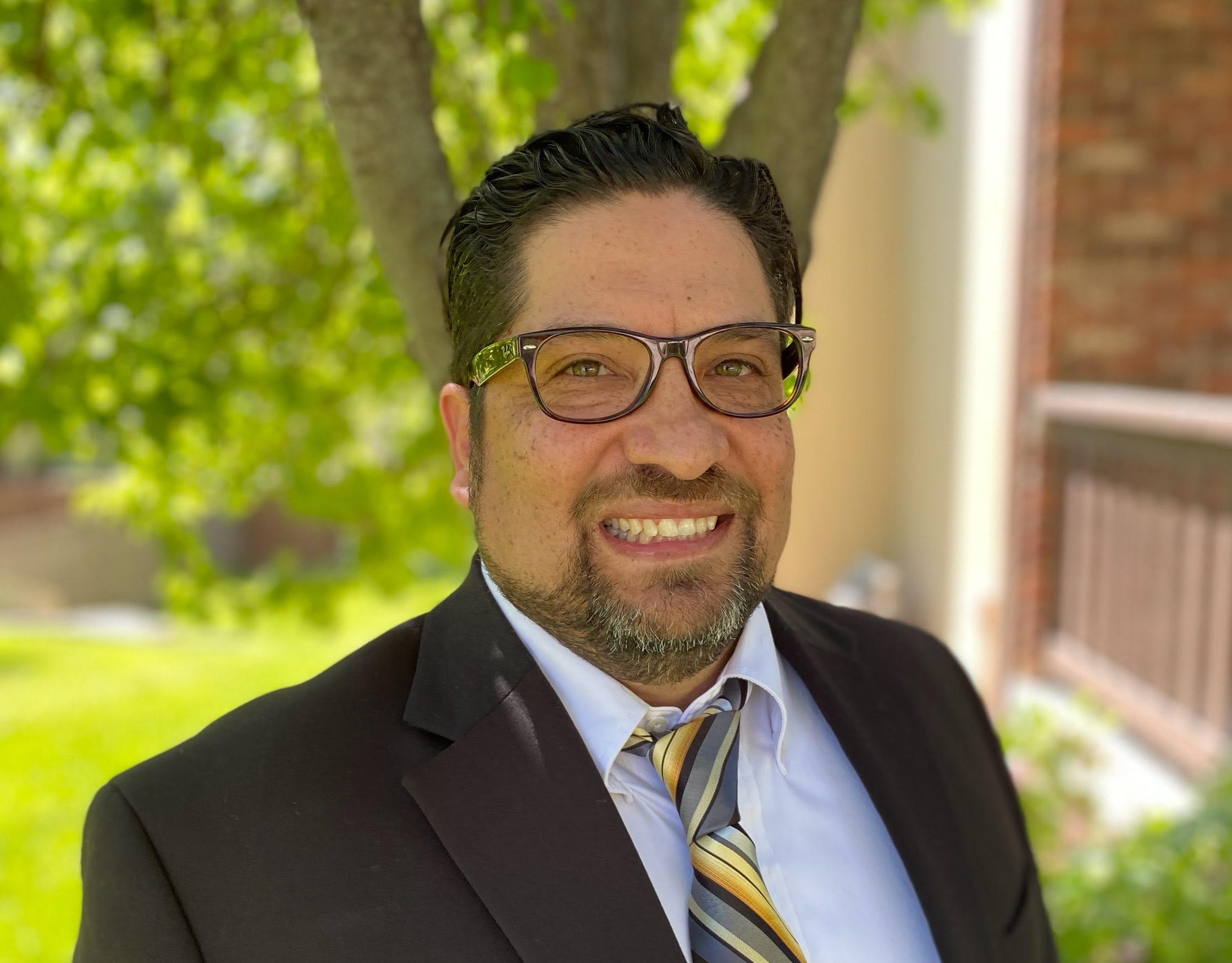 David Decker headshot taken outside with bright green trees behind him