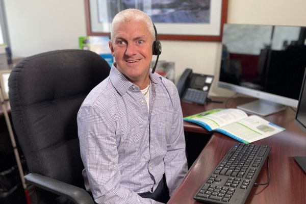 Andy Hoffman sitting at his desk, wearing a headset and smiling at the camera.