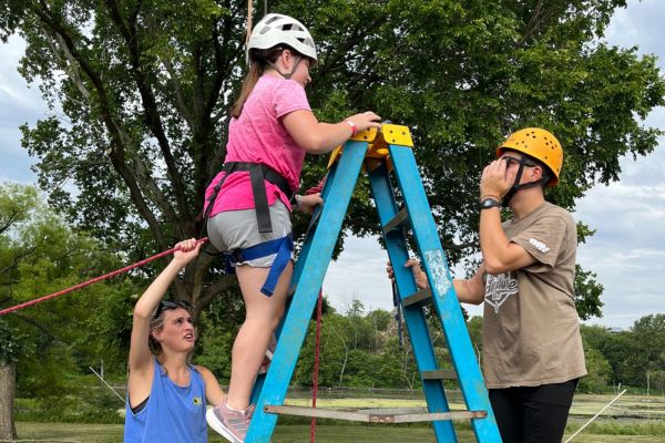 Two camp counselors putting a visually impaired girl into a harness before she rope swings.