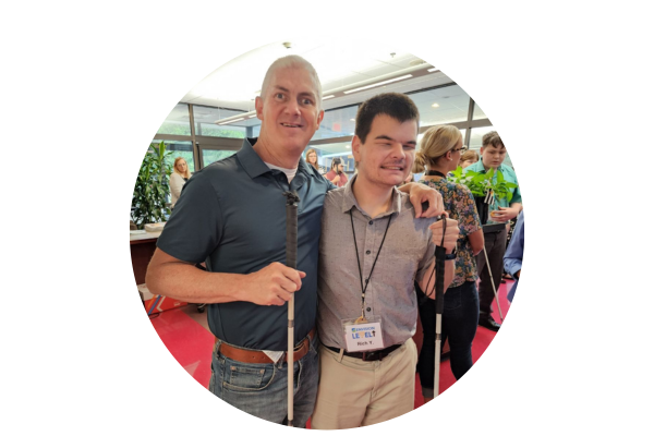Rich standing with Andy, an Envision employee, both holding their white canes and smiling,