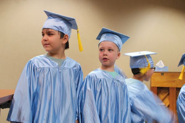 Two pre-k boys in their graduation caps and gowns, standing at the front of the room.