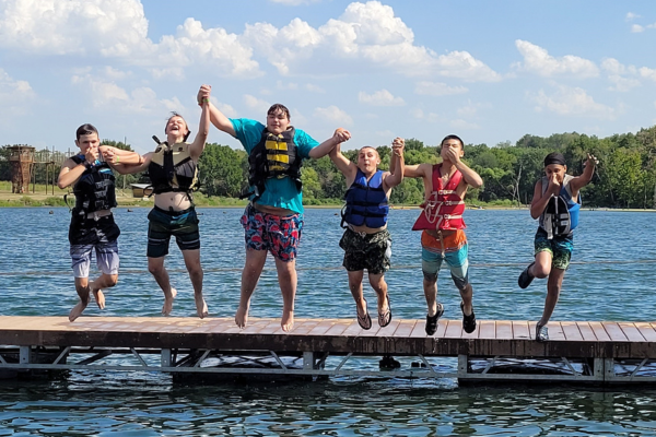 A group of kid jumping into the lake.