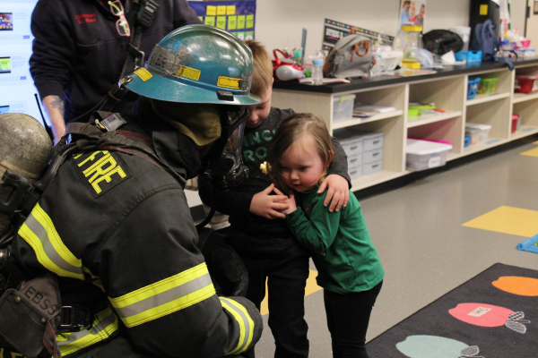 Two children touch the breathing apparatus on a firefighter in full uniform.