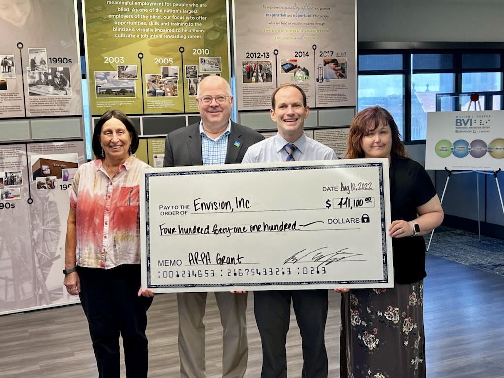 Three Envision employees standing with the City of Wichita Mayor holding a big check at the envision workforce innovation center