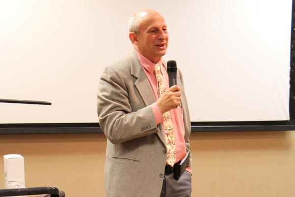 Dr. Fletcher standing at the front of a conference room speaking with a microphone in hand.