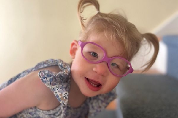 Charlotte wearing pink glasses with her hair styled in two pigtails, her face close up to the camera and she laughs while looking at the camera.