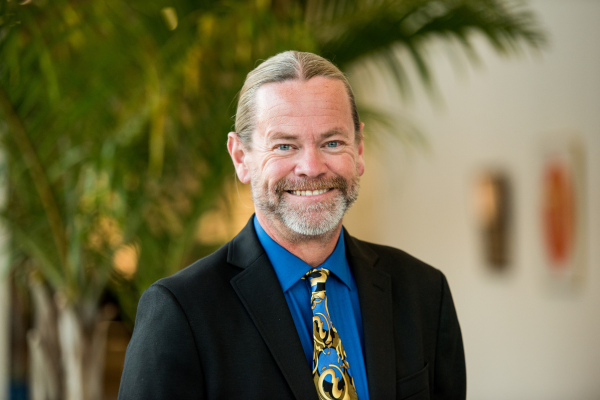 Michael Rodgers in a blue shirt and black suit, smiling brightly.