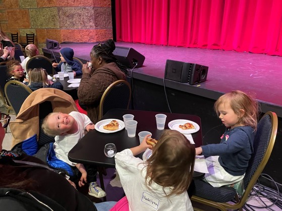 Two tables of children eating pizza in front of the stage at the children's theater center