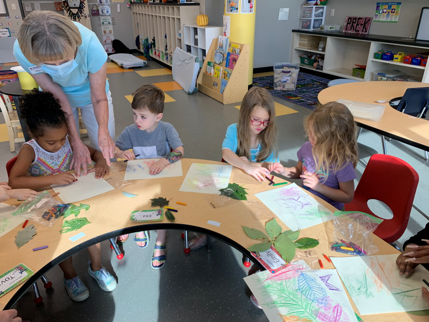 Preschool ECDC students sitting at table examining leaves