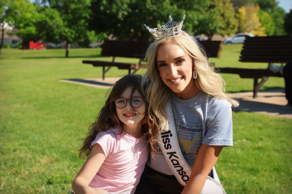 A Year of Service as Miss Kansas 2023 Courtney smiling as she wears her crown hugging a young child with glasses.