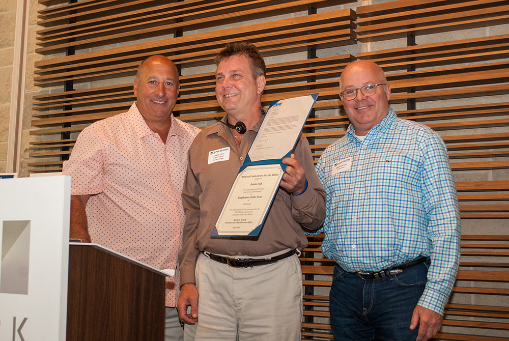 Michael Monteferrante, Jonas Voll, Mark Eaton stand on stage at luncheon while Jonas holds up his certificate