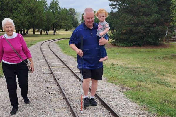 Bruce holding his grandson and walking with his white cane at Osage Park.