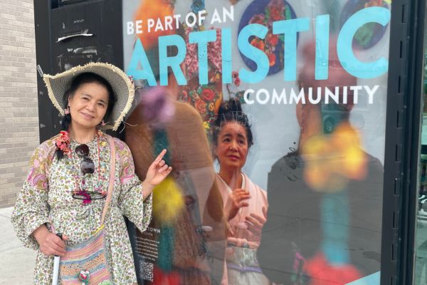 Tomiyo standing next to the bus stop art of her, pointing to it and smiling at the camera.