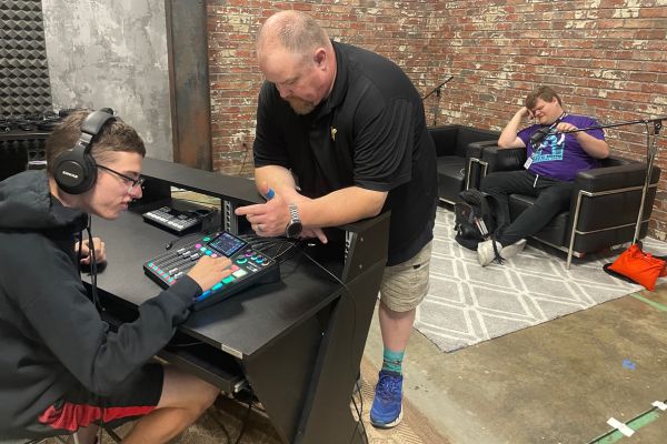 A volunteer putting a pair of headphones on a visually impaired teen inside Shocker Studios.