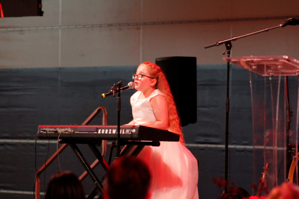 Emma on stage playing the piano and singing.