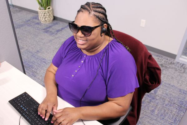 Laridda at her desk wearing a headset, typing on a keyboard and smiling.