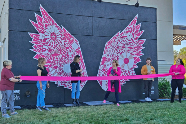 4 employees cutting a pink ribbon in front of the mural.