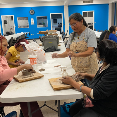 Jacinta teaching a group of women sculpting techniques by showing them how to mold clay.