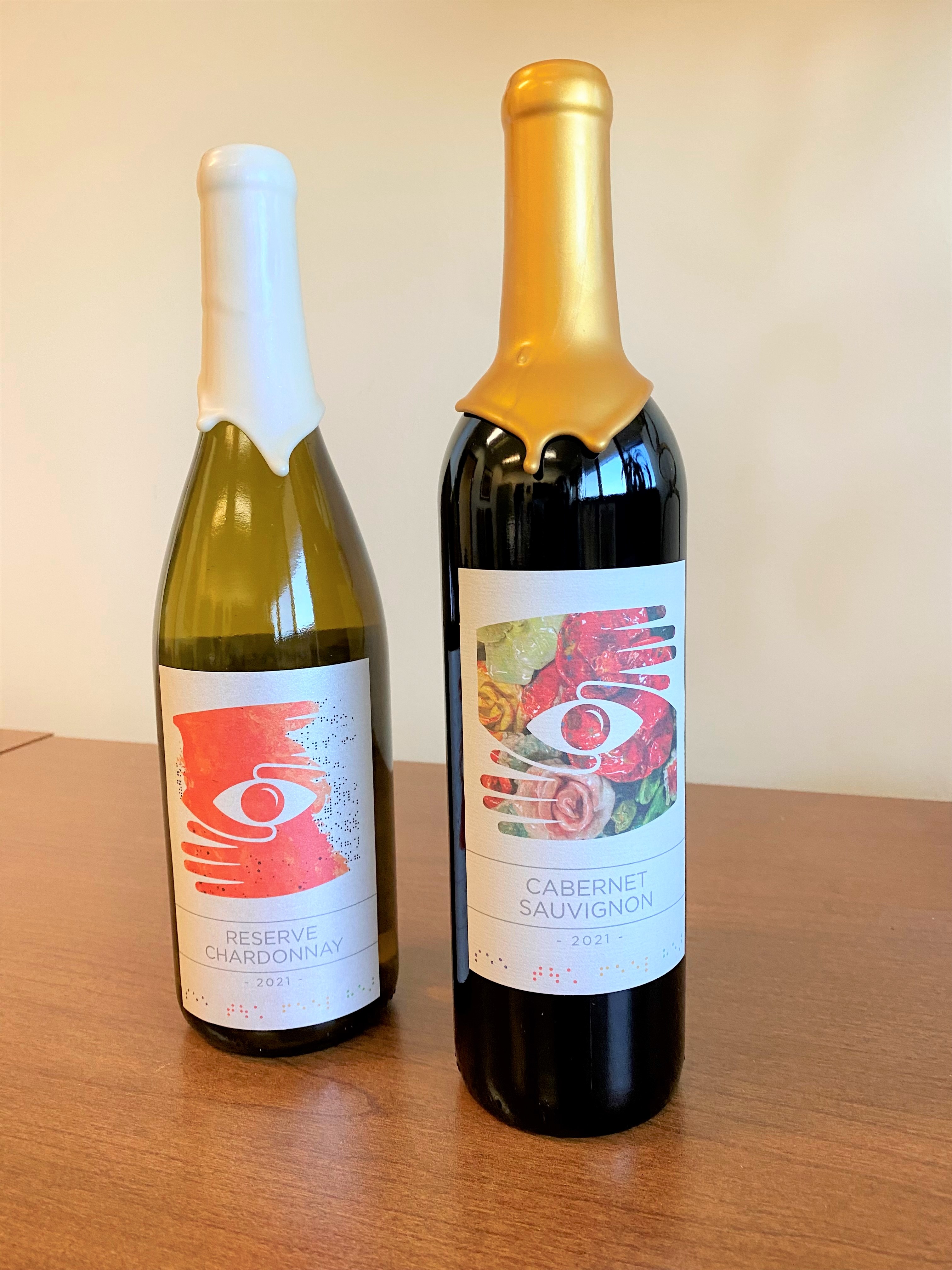 Two wine bottles with custom wine labels featuring the hand and eye logo of Envision made out of artwork imagery from Envision Arts artists
