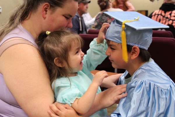 A pre-k graduate hugging his sister as she touches his graduation cap.