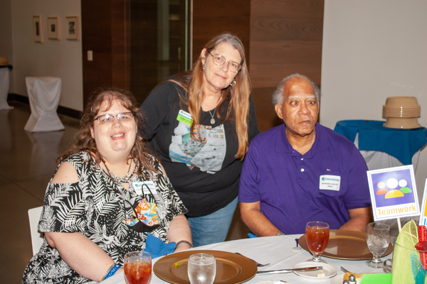 Dawn Dennis standing behind two PRIDE consumers who are sitting at a dinner table. 