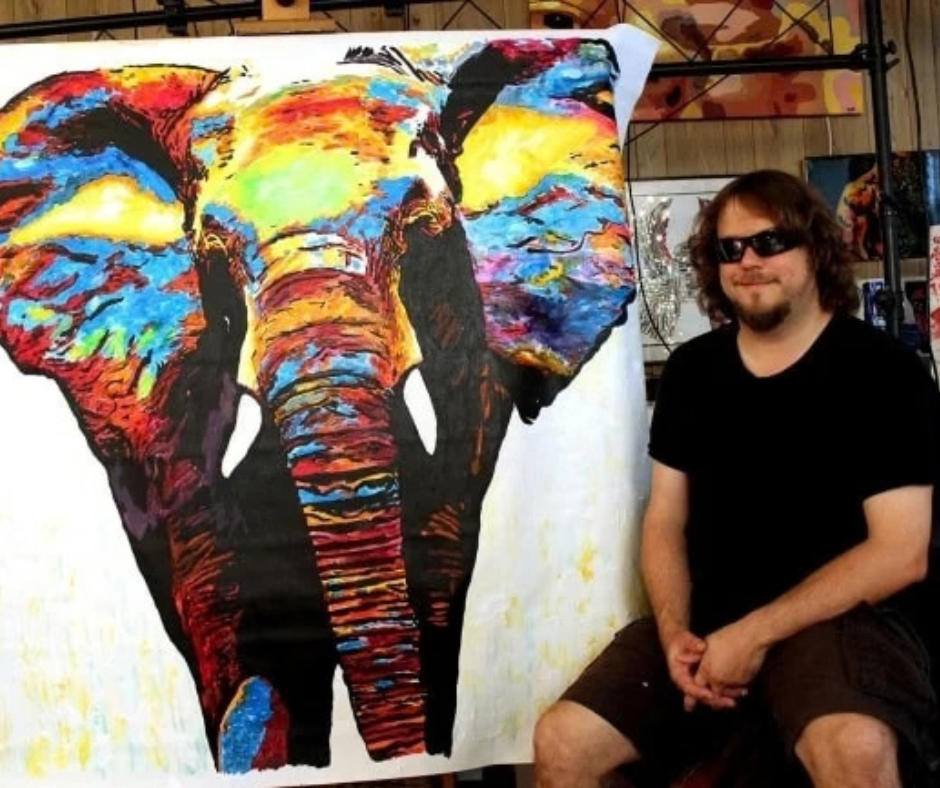 John Bramblitt sitting next to his piece of art 