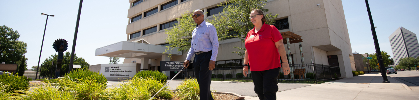 Envision rehab employee walking outside with patient using white cane in front of Envision building