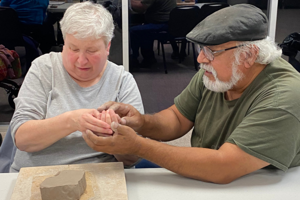 Tomas Bustos helps an Envision Dallas art student mold clay.