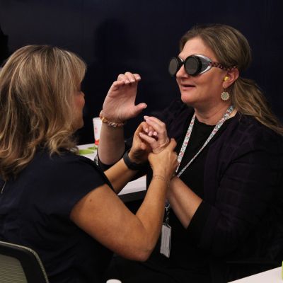 Two women learning, one with simulator glasses and one using sign language.