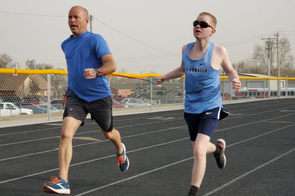 Caleb and his running guide Greg on the track together running, a band holding their wrists together.