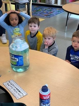 Four pre-k kids watch shaving cream in a jar of of water and food coloring