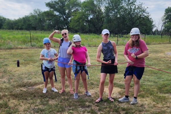 A group of 4 girls tugging on a rope, making funny faces at the camera.