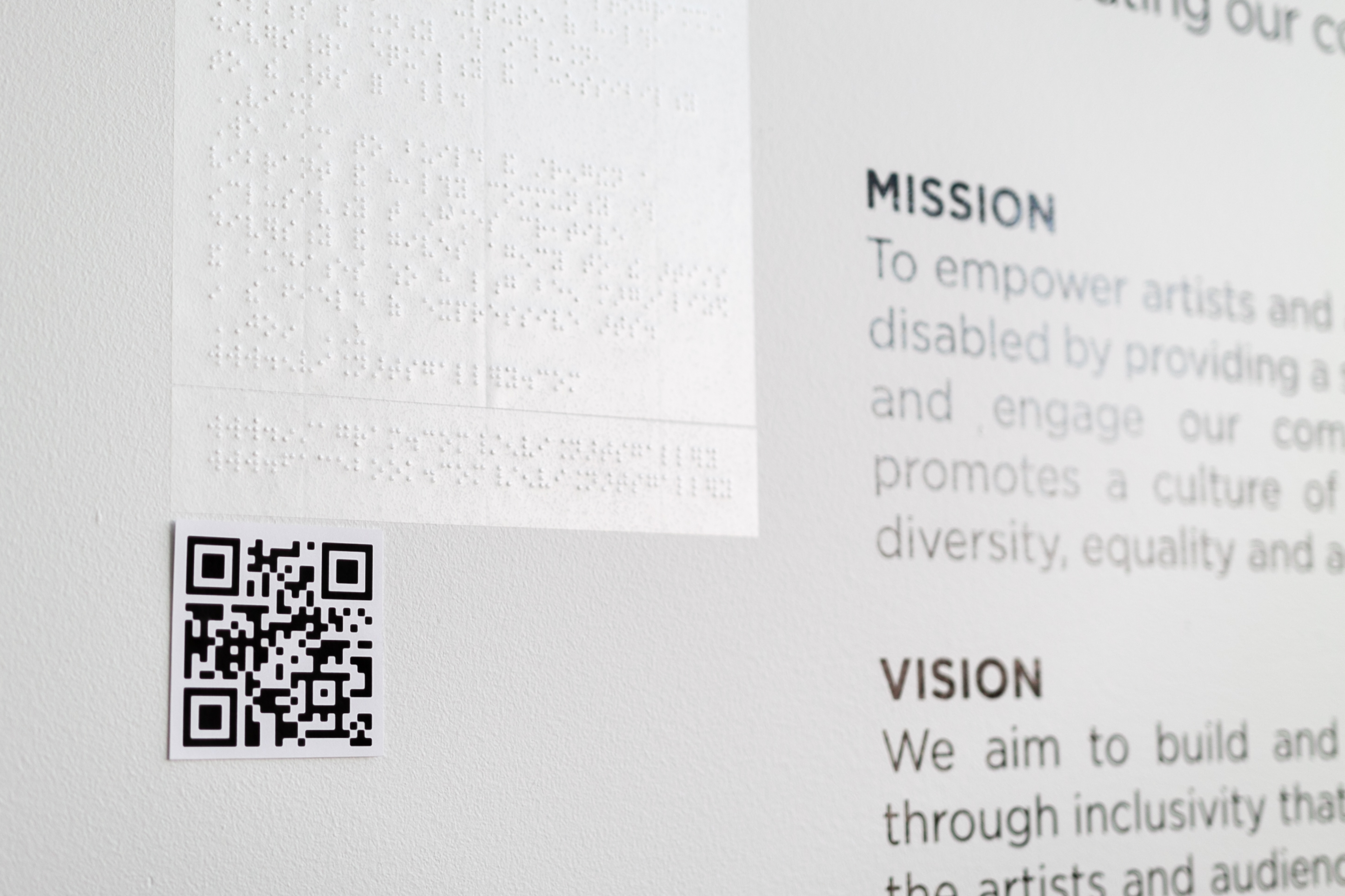 Envision Arts Gallery wall with mission state and information and then braille next to it with a QR code as well that leads to a PDF of the words on the wall