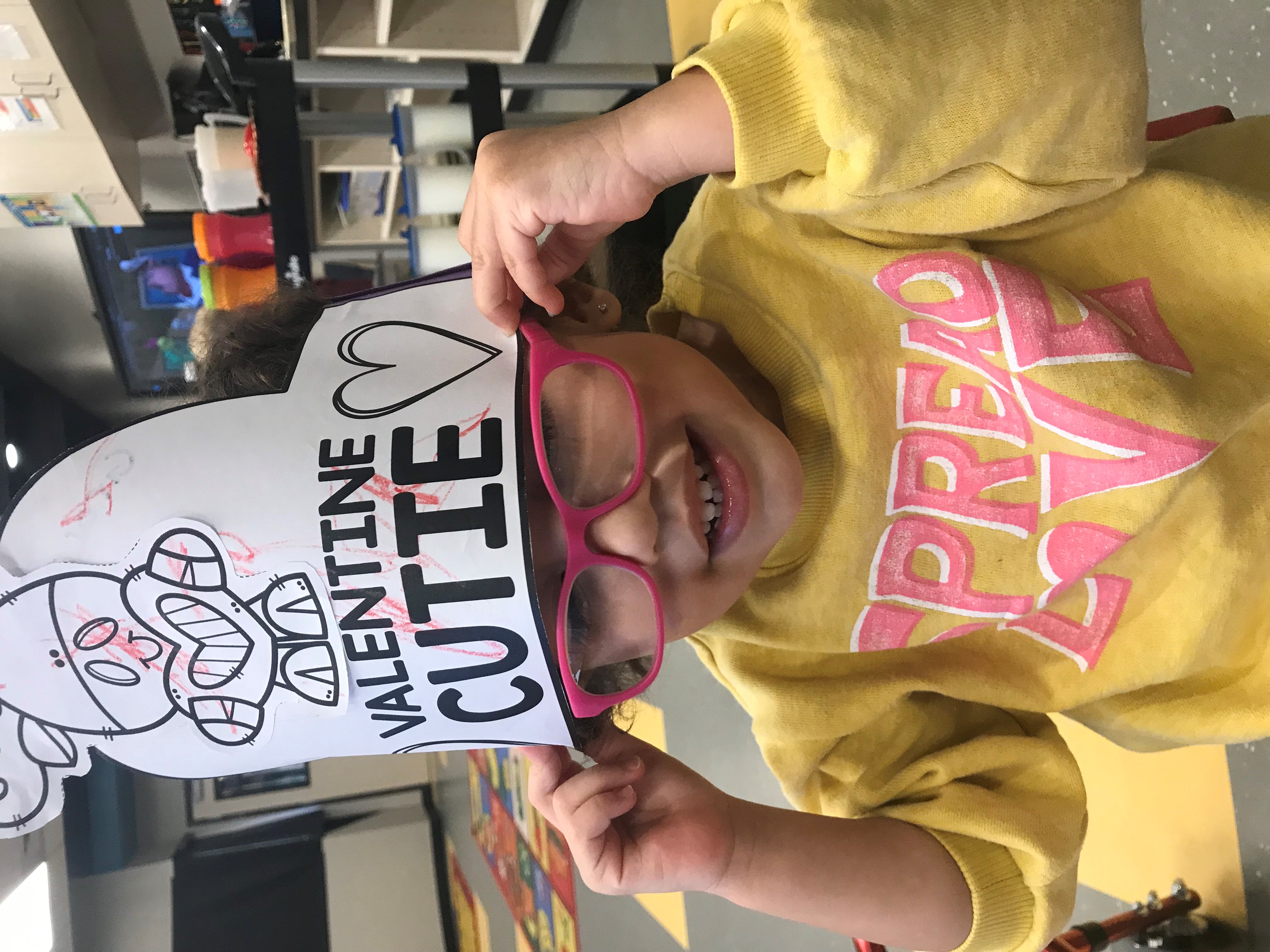 Grace smiling for the camera with a paper hat on her head that says "Valentine Cutie"