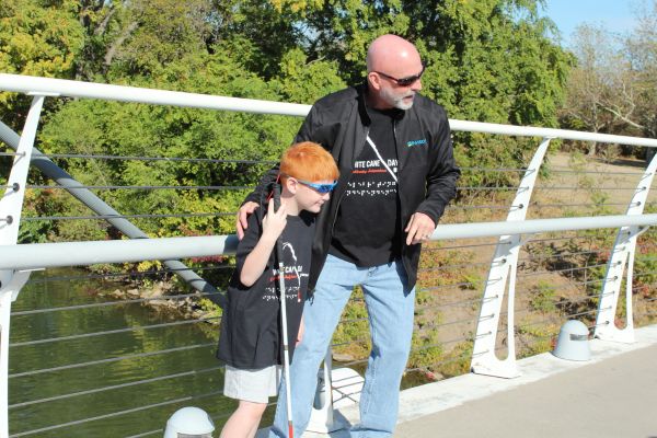Ray Oddis helping a young boy holding a white cane navigate across a bridge.