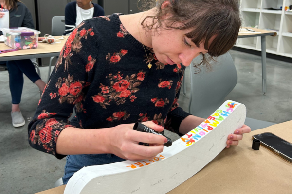 A young lady writing on a piece of wood in sharpie.