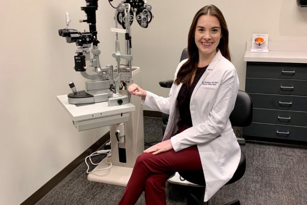 Dr. Burcham smiling brightly sitting next to eye exam equipment in her office within Envision Dallas.