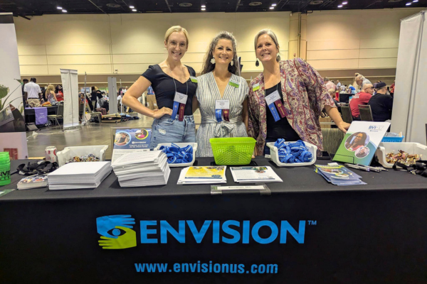 Chelsee, Courtney and Hannah standing behind the Envision booth smiling.