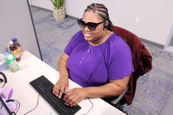 Laridda typing on a keyboard sitting at her desk, smiling brightly.