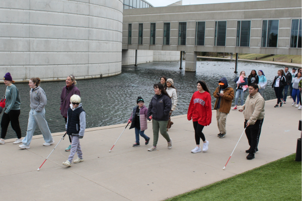 Around 50 people walking around the keeper of the plains, 3 in front with canes.