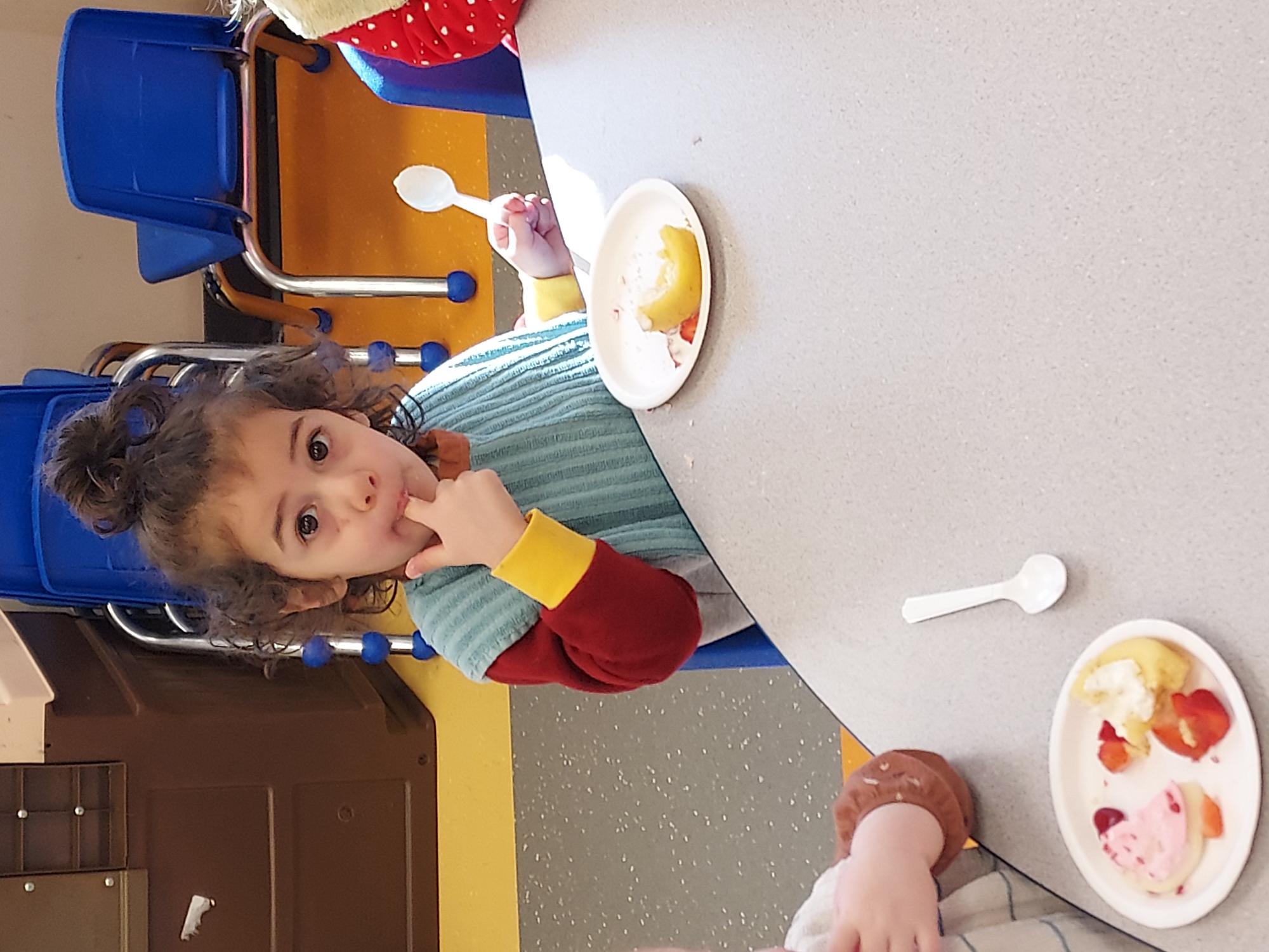 Photi sitting at a grey table eating strawberry shortcake.