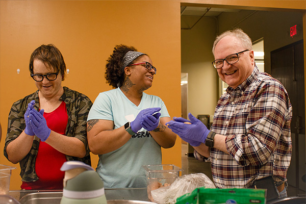 Adult rehabilitation participants laugh together as they prep food during a culinary skills class
