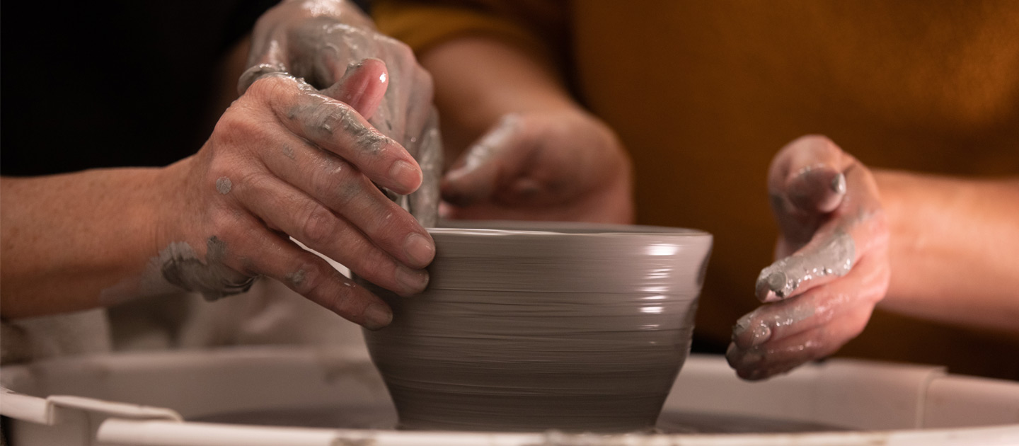 Artists shaping a bowl on the pottery wheel at the Envision Arts studio.