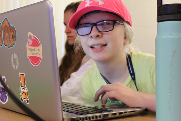 Lyra smiles at the camera as she works on her laptop at a Level Up session.