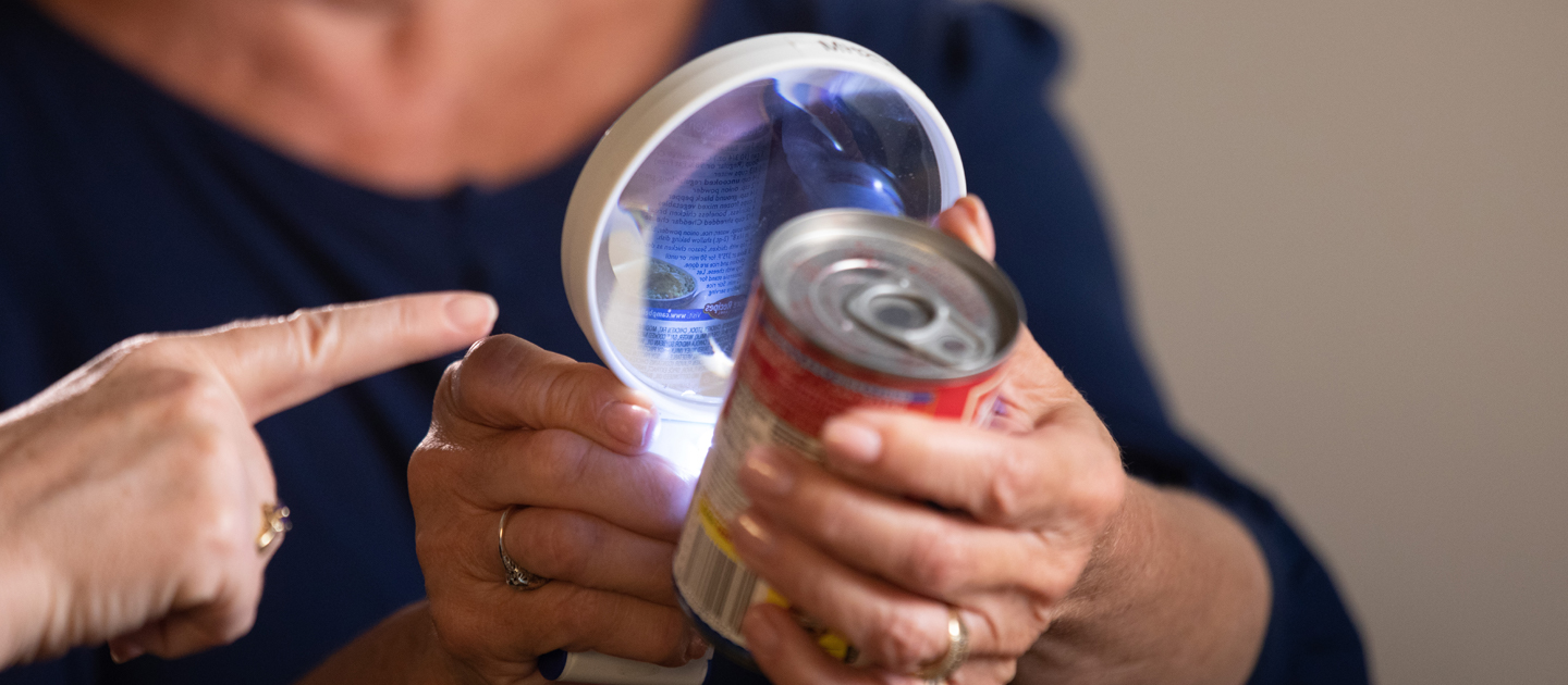 A client is shown how to use a lighted magnifying glass to read a can of soup.
