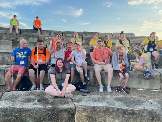 A big group of campers and counselors sitting outside on a rock stadium around a fire pit